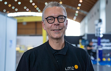 Ein Mann, der Mitarbeiter am Landesmedienzentrum ist mit grauen Haaren und Brille laechelt in die Kamera.