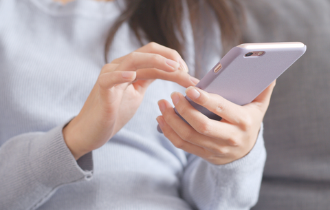 Ein Smartphone steht im Zentrum des Bildes. Eine Frau hält es in den Händen und tippt darauf.