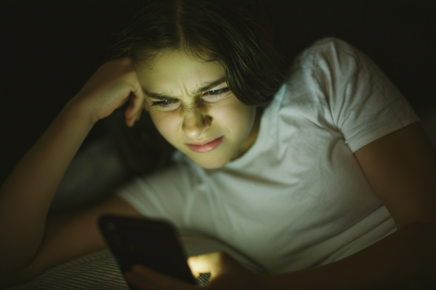 Junge Frau schaut kritisch auf ein Smartphone.