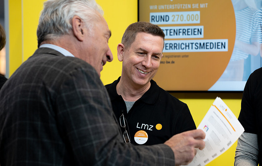 Zwei Männer lachen und schauen auf ein Blatt Papier.