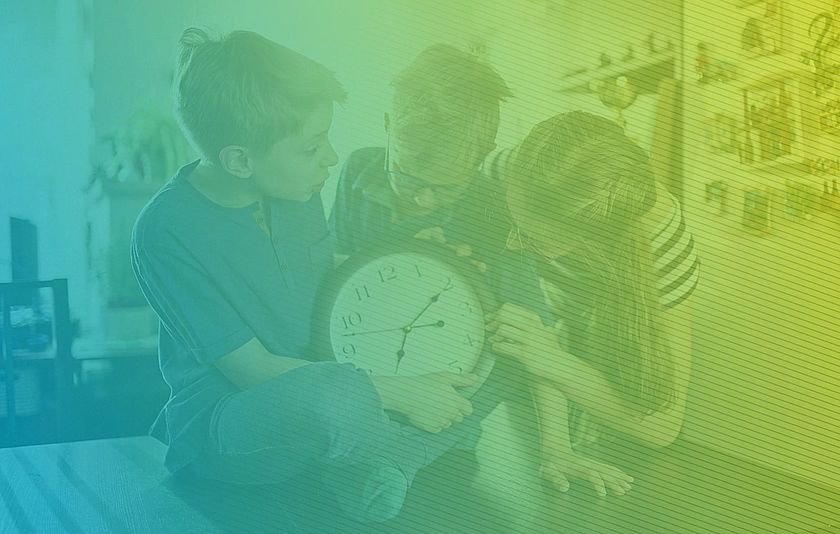 Drei Kinder schauen auf eine Uhr.