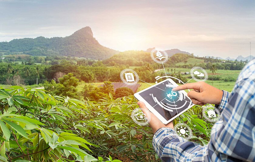 Person mit Tablet in der Hand steht vor einer hügeligen Landschaft.