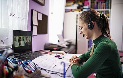 Frau mit Headset vor dem Laptop bei einer Videokonferenz