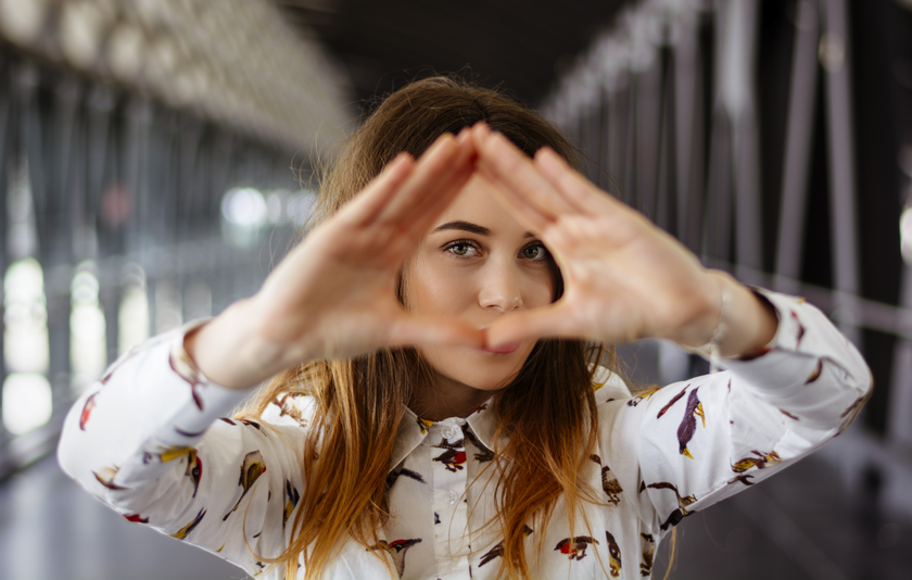 Eine junge Frau formt mit beiden Händen ein Dreieck und hält dieses vor ihr rechtes Auge.