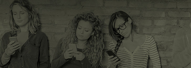 Jugendliche stehen nebeneinander vor einer Wand und schauen auf ihre Smartphones.