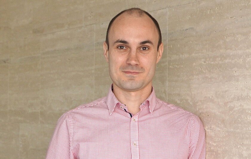 Ein Mann mittleren Alters mit dunklen Haaren und hellrotem Hemd blickt freundlich in die Kamera.