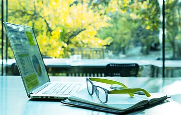 Laptop, Buch und Brille auf einem Schreibtisch