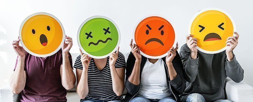 Personen halten sich negative Emojis vor ihre Gesichter Personen halten sich negative Emojis vor ihre Gesichter