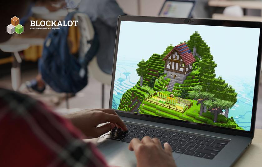 Hände liegen auf einem aufgeklappten Laptop, auf dem eine Berglandschaft mit Haus aus quadratischen Blöcken zu sehen ist. 