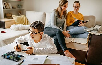 Junge mit Smartphone beim Schreiben an einem Tisch