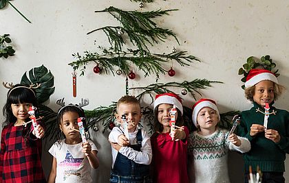 Kinder mit Nikolausmützen vor einer Wand mit Tannenzweigen