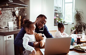 Ein Mann, der mit seinen Kindern am Tisch sitzt und von zuhause aus arbeitet