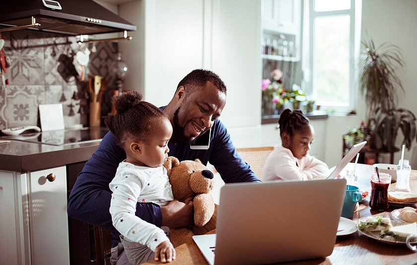 Ein Mann, der mit seinen Kindern am Tisch sitzt und von zuhause aus arbeitet