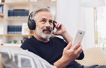 Älterer Mann hört mit Kopfhörer etwas vom Smartphone.