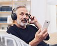Älterer Mann hört mit Kopfhörer etwas vom Smartphone.