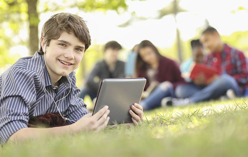 Junge mit Tablet liegt auf Gras