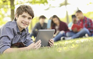 Junge mit Tablet liegt auf Gras