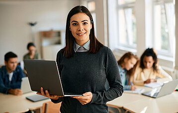 Junge Lehrerin mit Laptop in einer Schulklasse.