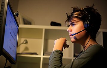 Ein Junge mit Headset sitzt konzentriert am Computer