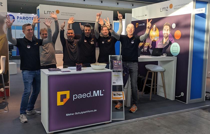 Das Standpersonal des paed.ML-Teams jubelt auf der Messe fröhlich in die Kamera.