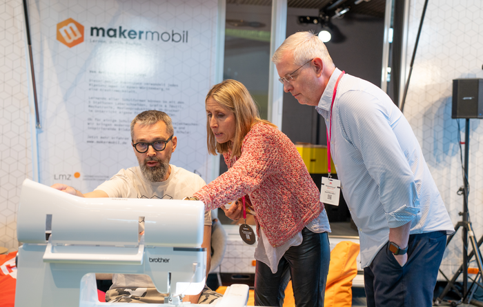 Drei Personen stehen an einer Stickmaschine vor dem Makermobil