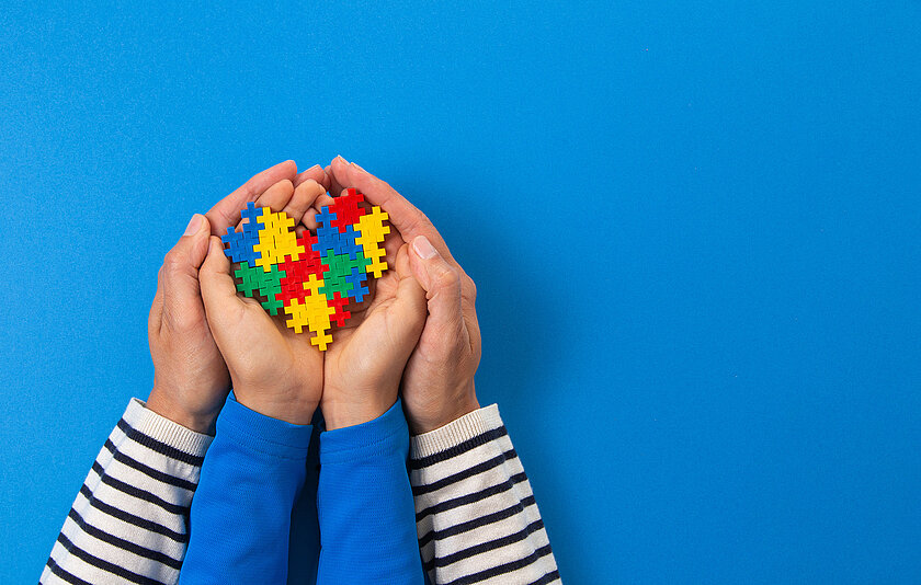 Hände eines Erwachsenen und eines Kindes halten gemeinsam ein Herz aus Puzzleteilen.