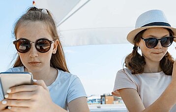 Teenagerinnen mit Smartphones unter Sonnenschirm