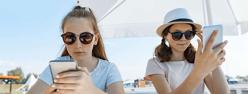 Teenagerinnen mit Smartphones unter Sonnenschirm