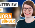 Links steht der Text:Interview mit Nora Buenger. Rechts sieht man Nora Buenger, eine Frau mit braunen kuerzeren Haaren und Brille, die laechelt.