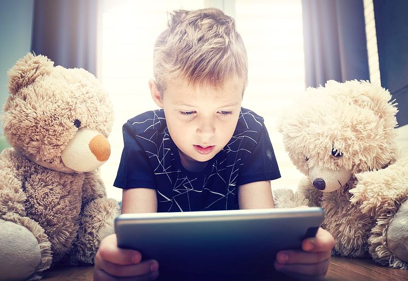 Junge schaut mit zwei Teddys auf ein Tablet