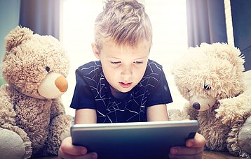 Junge schaut mit zwei Teddys auf ein Tablet