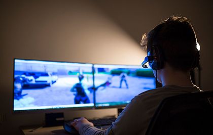 Ein Junge mit einem Headset sitzt vor zwei Bildschirmen und spielt ein Multiplayer Online Game