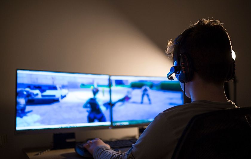Ein Junge mit einem Headset sitzt vor zwei Bildschirmen und spielt ein Multiplayer Online Game