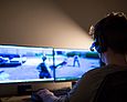 Ein Junge mit einem Headset sitzt vor zwei Bildschirmen und spielt ein Multiplayer Online Game