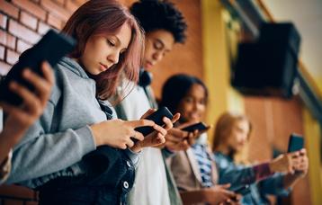 Jugendliche mit Smartphone in der Hand in einem Schulgebäude. 