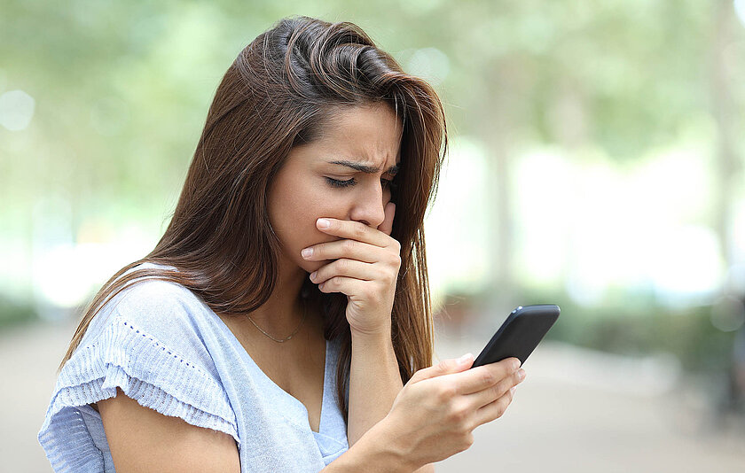 Jugendliche schaut geschockt und ängstlich auf ihr Smartphone.