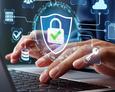 Man sieht einen aufgeklappten Laptop, darüber tippende Hände. Über dem Foto lagert eine Grafik mit einem Sicherheitsschloss, ein Symbol für eine Firewall.