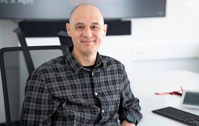 Alfred Wackler sitzt lächelnd an seinem Schreibtisch und stellt sich Interviewfragen.