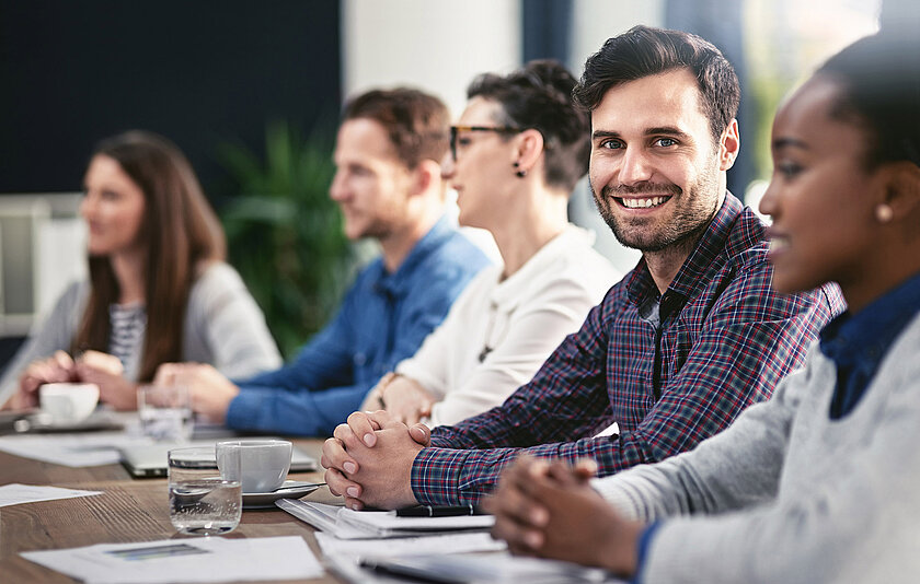 Junge Erwachsene in einer Schulung. Ein Teilnehmer lächelt freundlich in die Kamera.