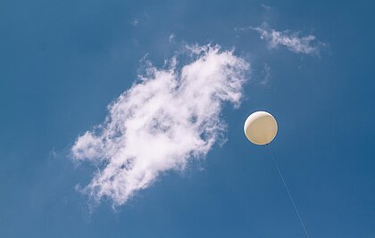 Wetterballon fliegt in den blauen Himmel einer Wolke entgegen.