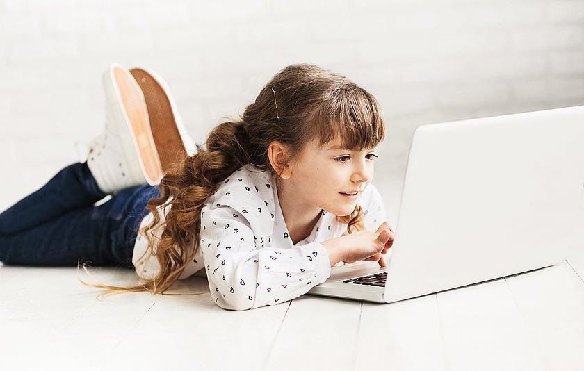 Mädchen liegt vor einem Laptop auf dem Boden