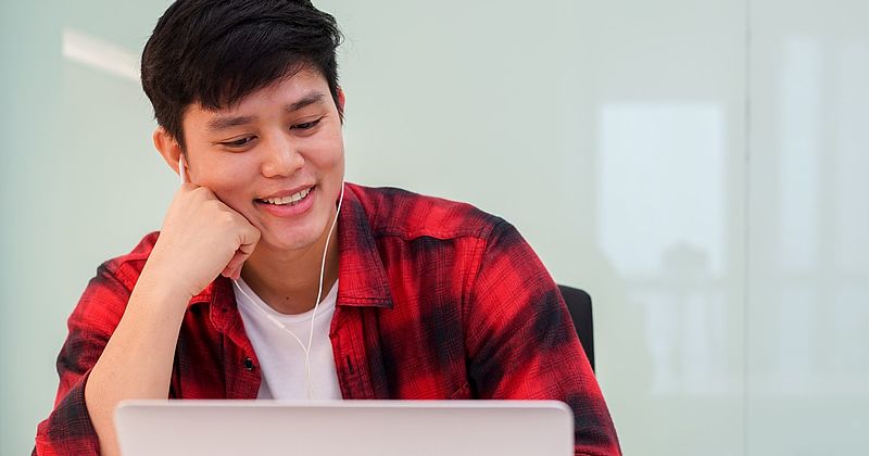 Teenager sitzt lächelnd und mit Kopfhörer vor einem Laptop