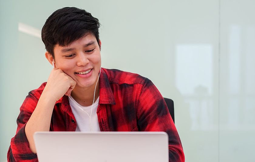 Teenager sitzt lächelnd und mit Kopfhörer vor einem Laptop
