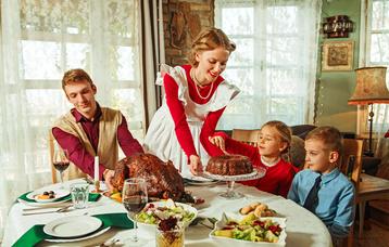 50er Jahre: Familie am Tisch. Frau mit rotem Kleid und Schürze serviert das Thanksgiving-Mahl.