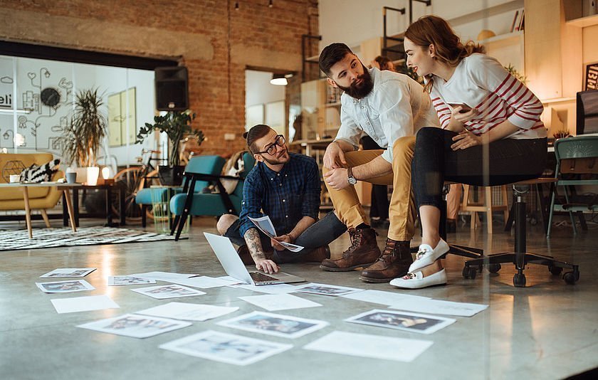 Junge Menschen sprechen über Bilder, die vor ihnen auf dem Boden liegen