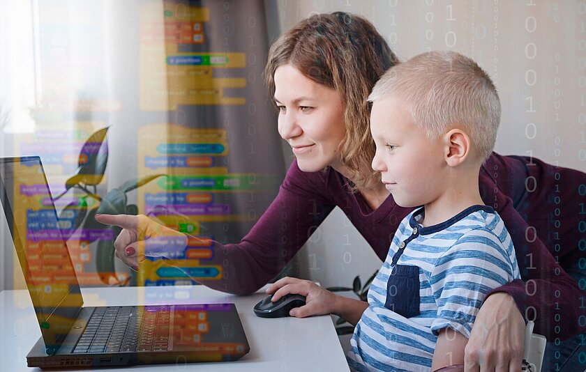Eine Frau lehnt sich zu einem Jungen im Grundschulalter herunter, der an einem Laptop sitzt und auf eine Maus klickt. Im Hintergrund sind als Schattierungen bunte Kästen mit Text sowie Nullen und Einsen zu sehen.  