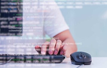 Hand auf PC-Tastatur mit eingeblendeter Programmiersprache