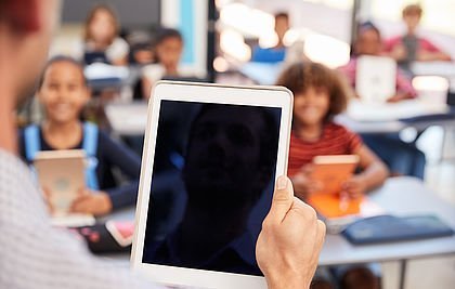 Hand hält Tablet vor einer Schulklasse