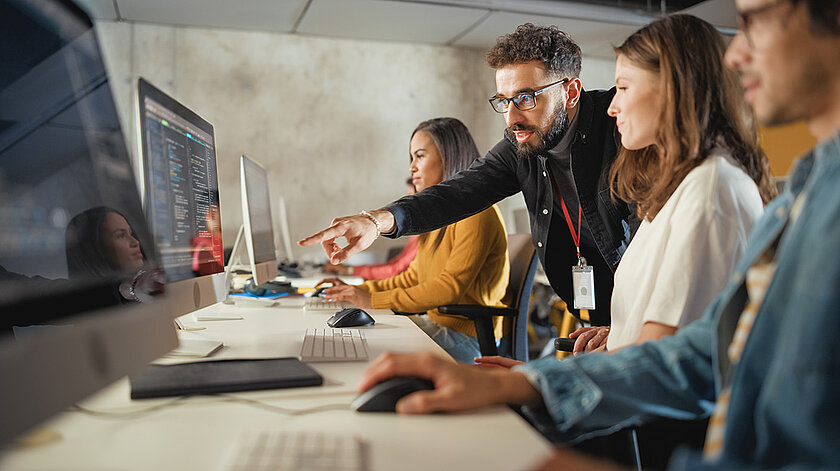 Lehrkraft zeigt Schülerinnen und Schülern etwas am Computer.