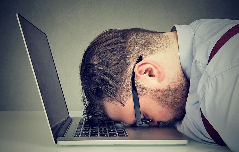 Mann schläft vor Laptop ein Ein Mann hat seinen Kopf auf einen Laptop gelegt und schläft